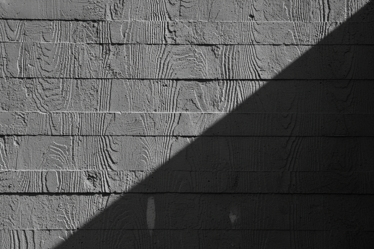 An abstract close-up of raw board-formed concrete, the grain of the wooden formwork visible across the surface under dramatic raking shadow.