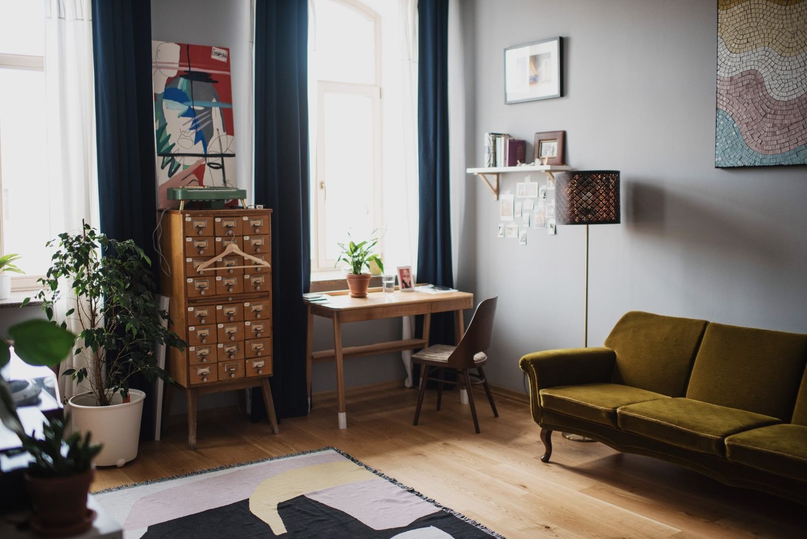 Living room with a green sofa, wooden floor, plants and framed artwork