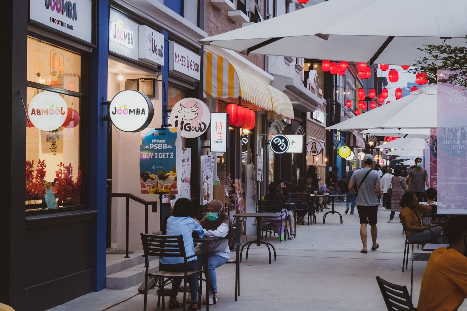 Row of illuminated shopfronts along a city sidewalk in the evening