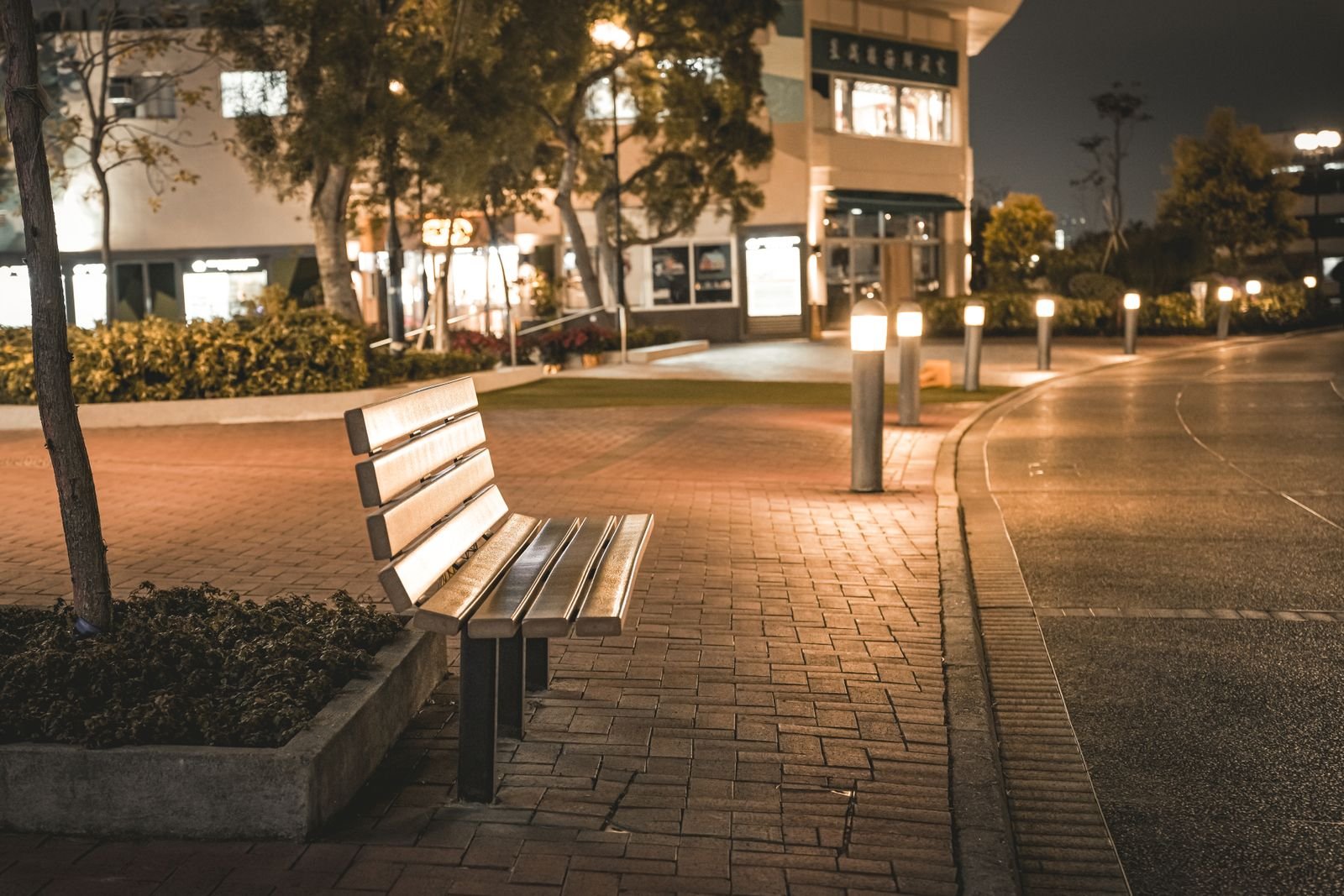 Empty public bench beside illuminated bollards on a city sidewalk at night