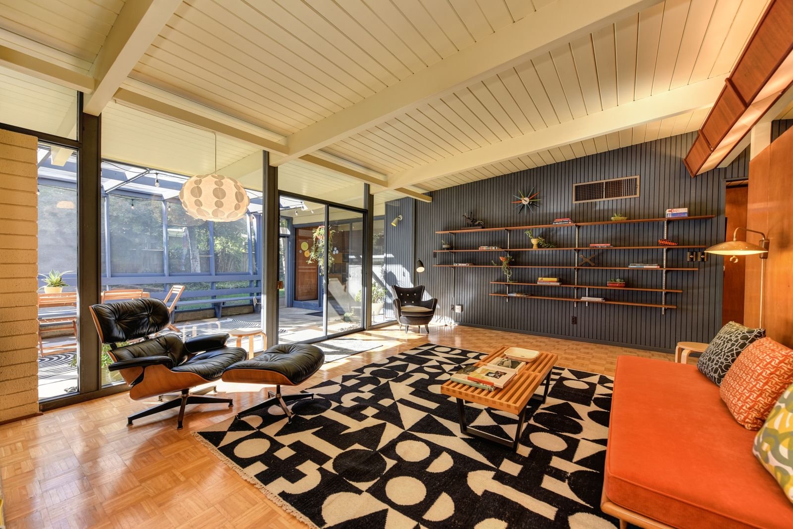 Mid-century modern living room with wooden armchairs, open shelving and natural light