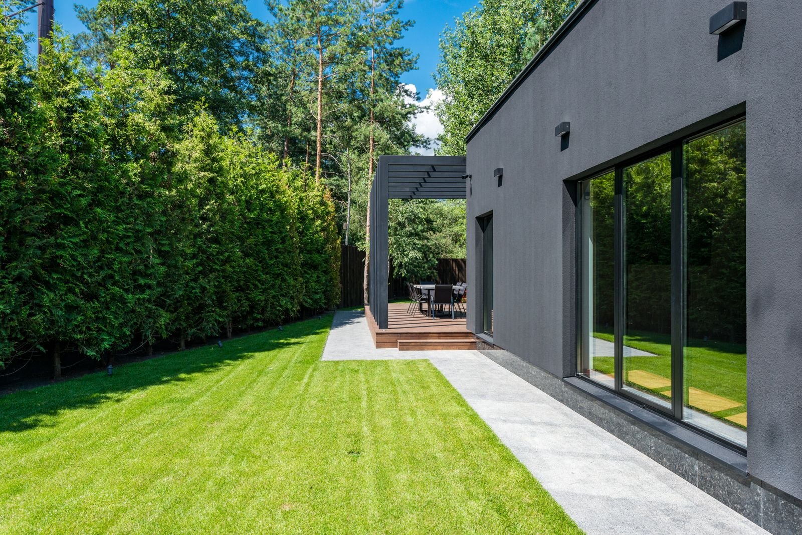 Modern house exterior with large windows, a lawn and outdoor seating area