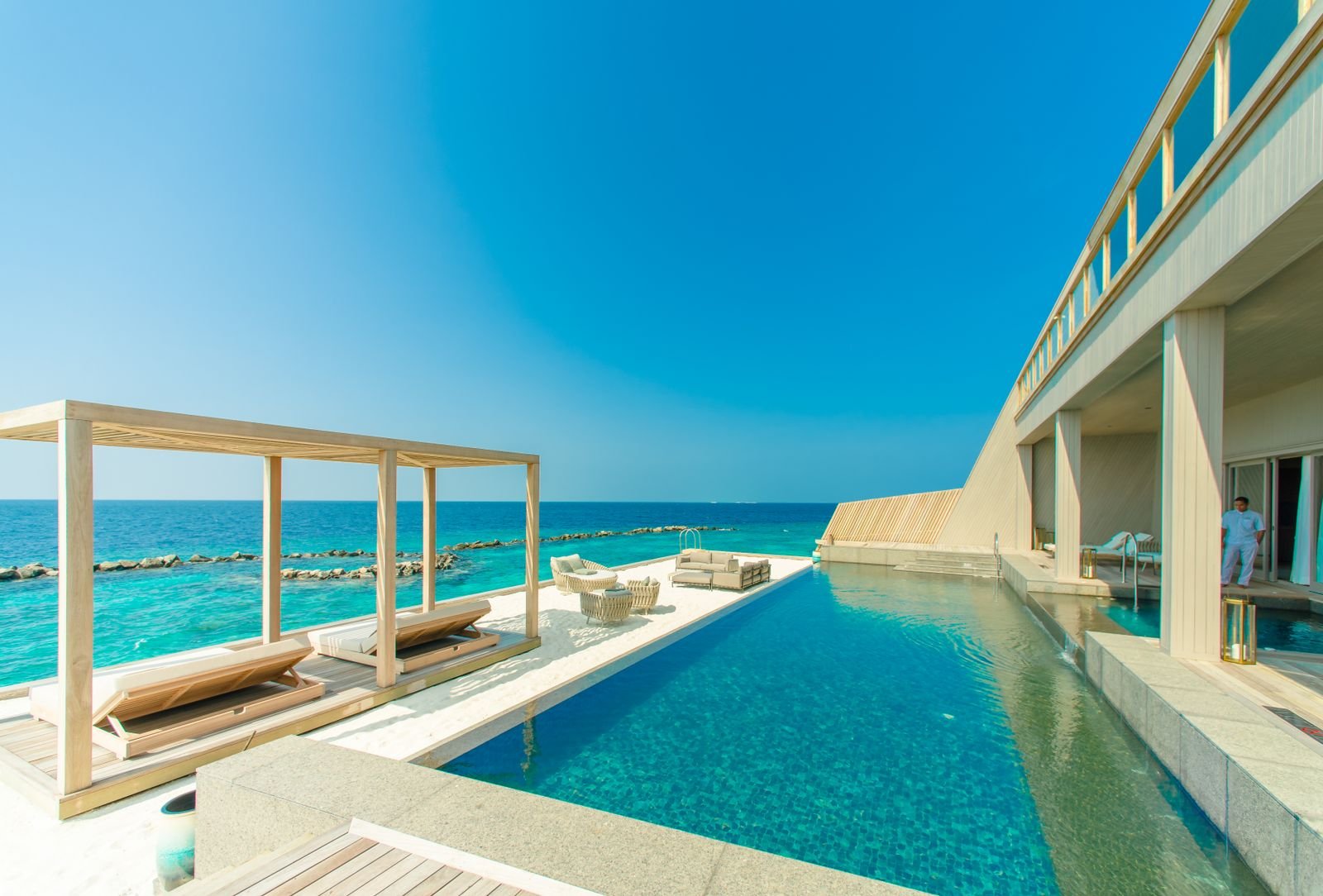 Infinity pool and outdoor lounge chairs overlooking the ocean at a beachside resort