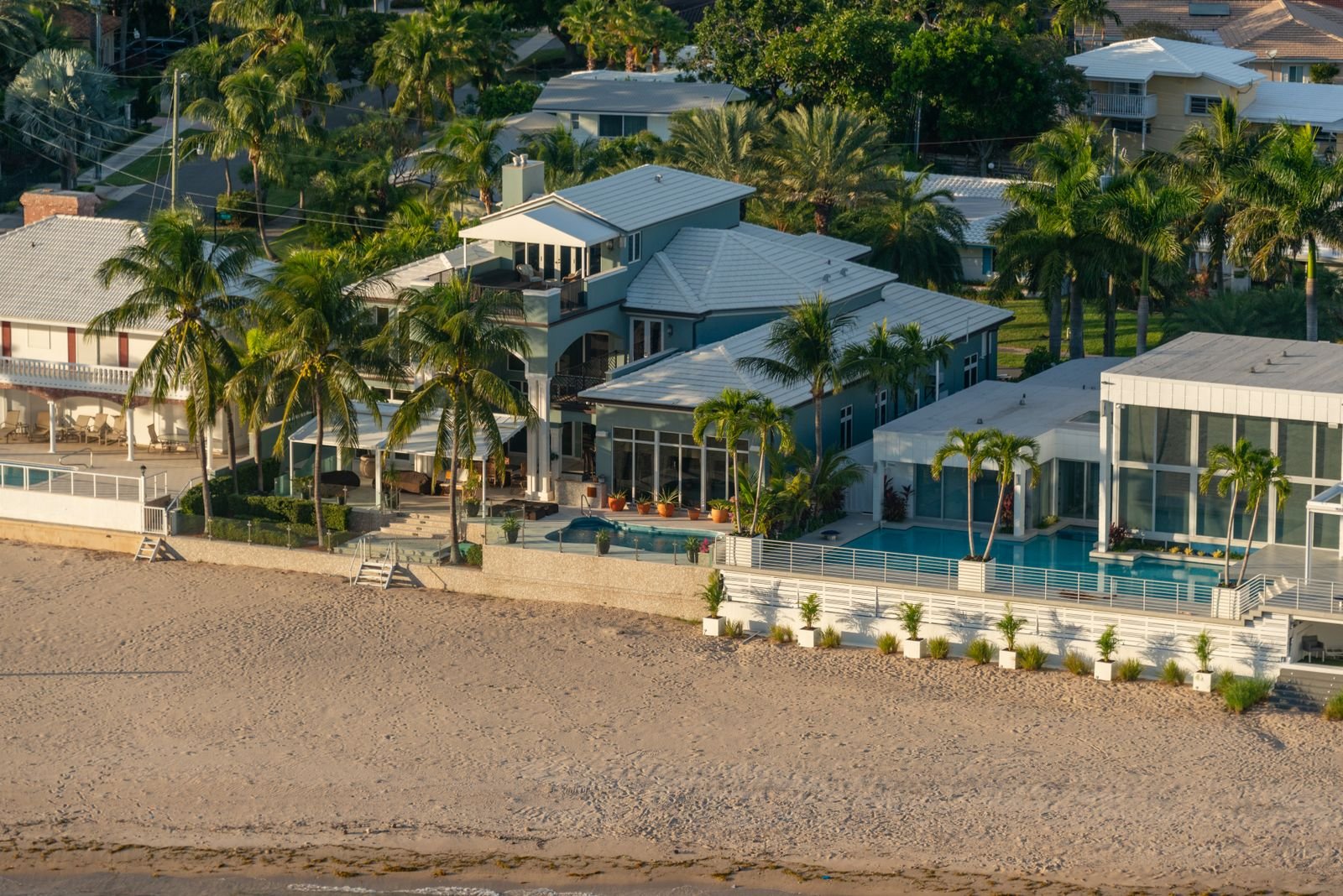 Aerial view of beachfront resort villas with palm trees and a pool beside the sand