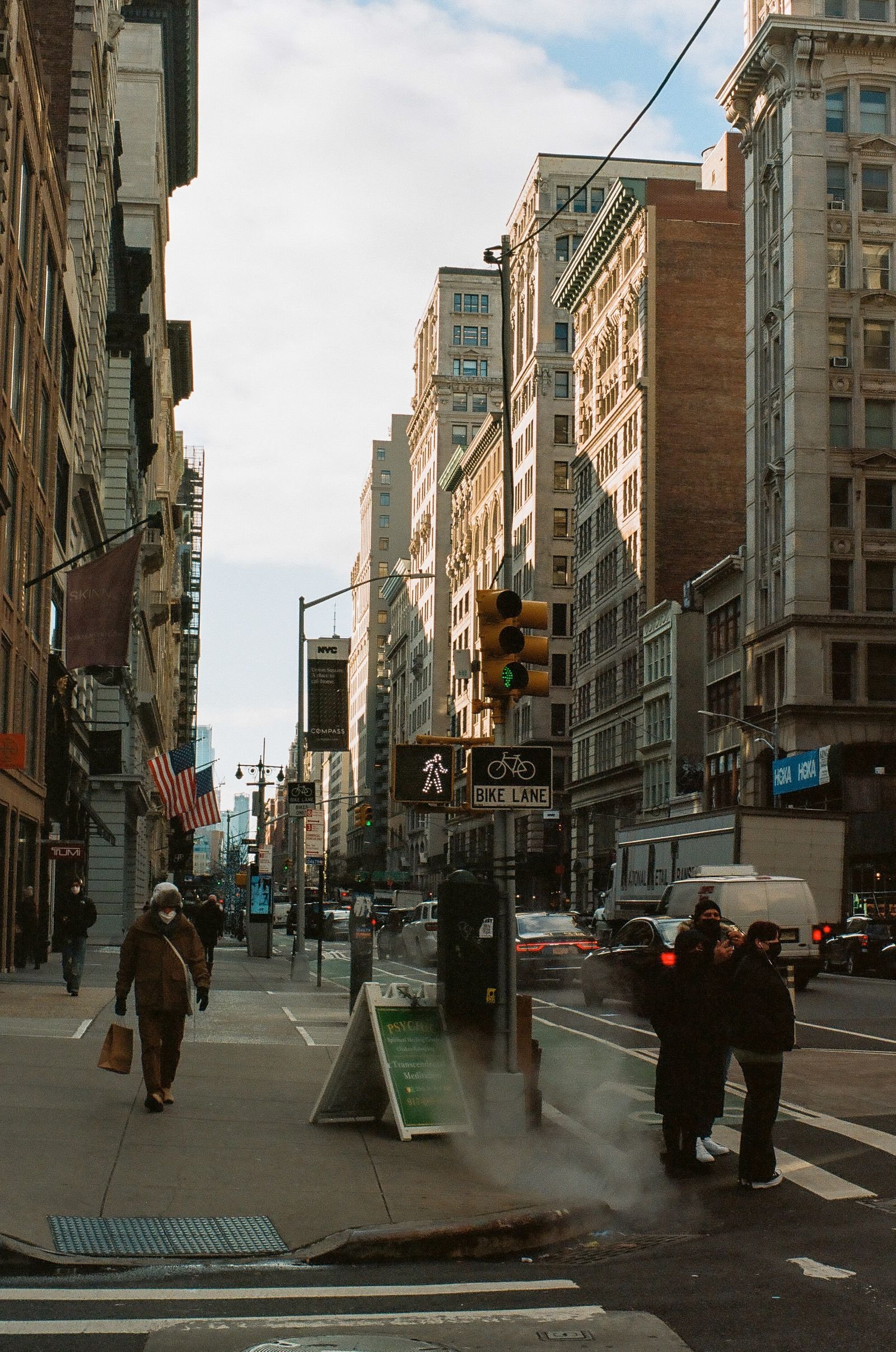 City sidewalk lined with shopfronts and pedestrians in low winter sunlight